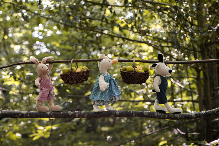 Three stuffed animals on a branch with fruit baskets against a natural background