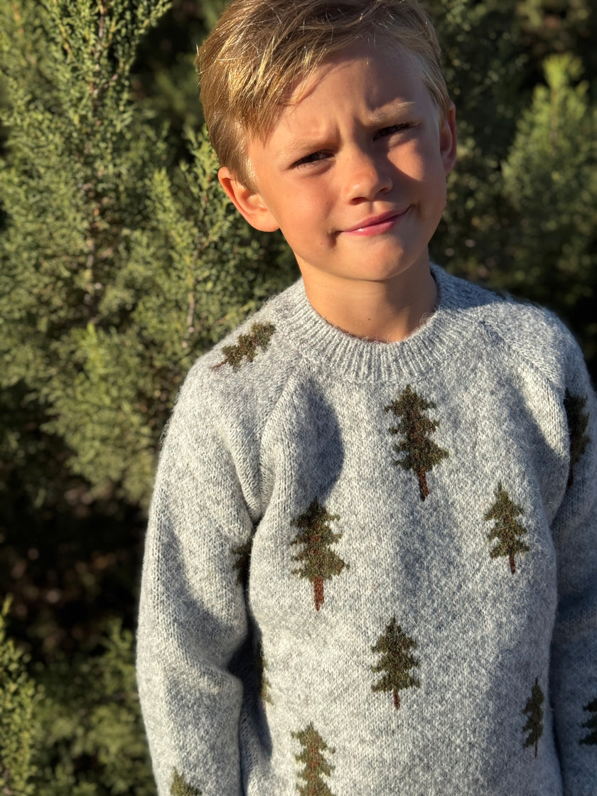 Child wearing a sweater with tree patterns outdoors