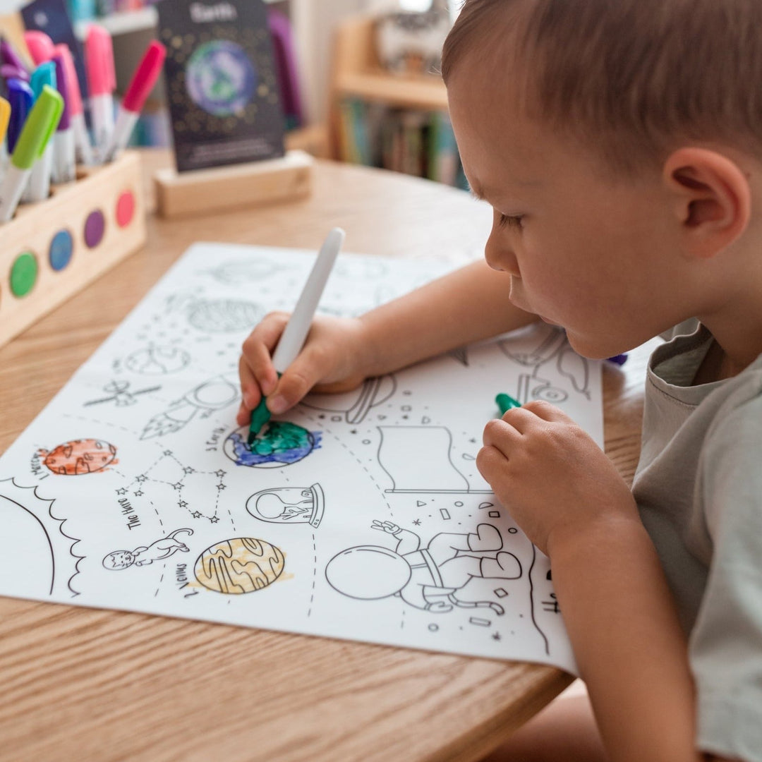 Child coloring a space-themed picture with markers on a wooden table.