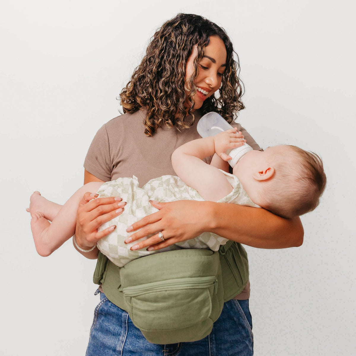 Woman holding a baby and feeding it with a bottle against a plain background