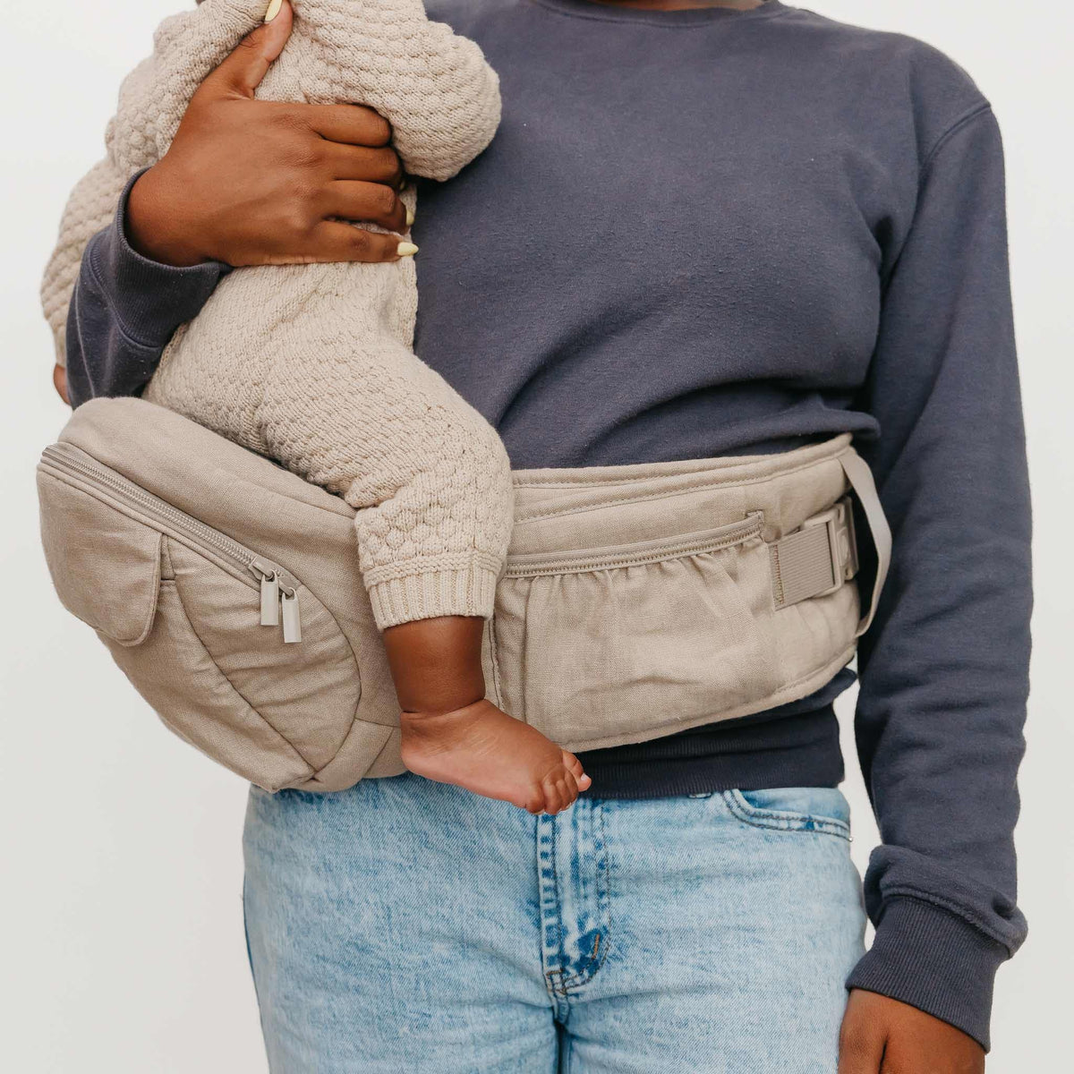 Person holding a baby in a beige baby carrier against a plain background