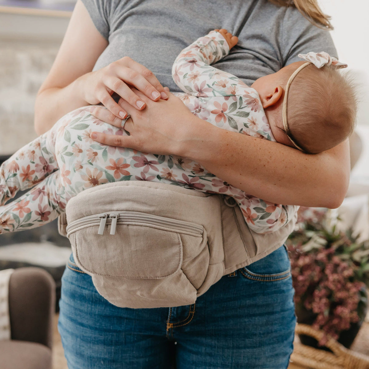 Woman holding a baby in a carrier with a blurred indoor background