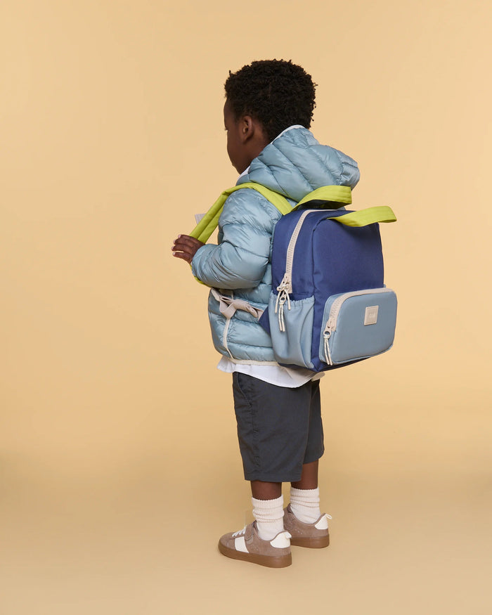 Child wearing a blue and green backpack on a beige background