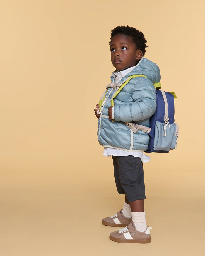 Child wearing a blue jacket and backpack on a beige background