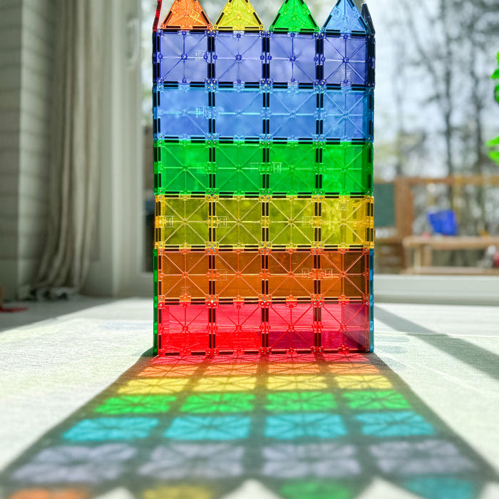 A tall tower built from colorful, translucent Magna-Tiles casting a vibrant rainbow pattern across the floor.