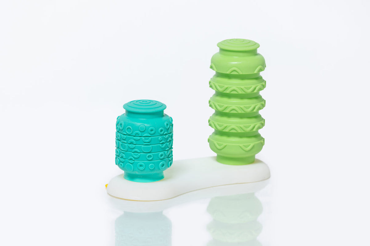 Two textured silicone cups, one green and one blue, on a white base with a light gray background.