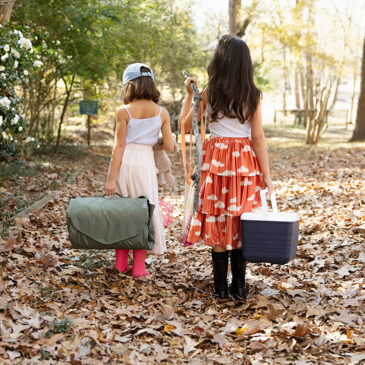 Two children with a suitcase and picnic basket in a forest setting