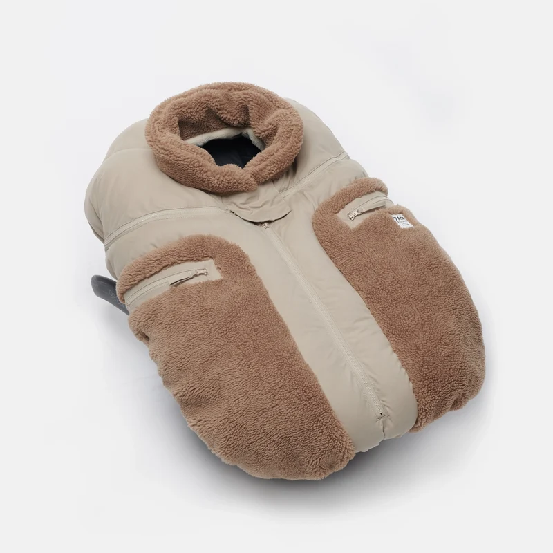 Benji Applique Car Seat Cocoon by 7AM Enfant featuring a close-up of the light taupe or oat-colored weatherproof outer shell, brown sherpa fleece trim around the collar and zippered side pocket, and a front zipper detail.