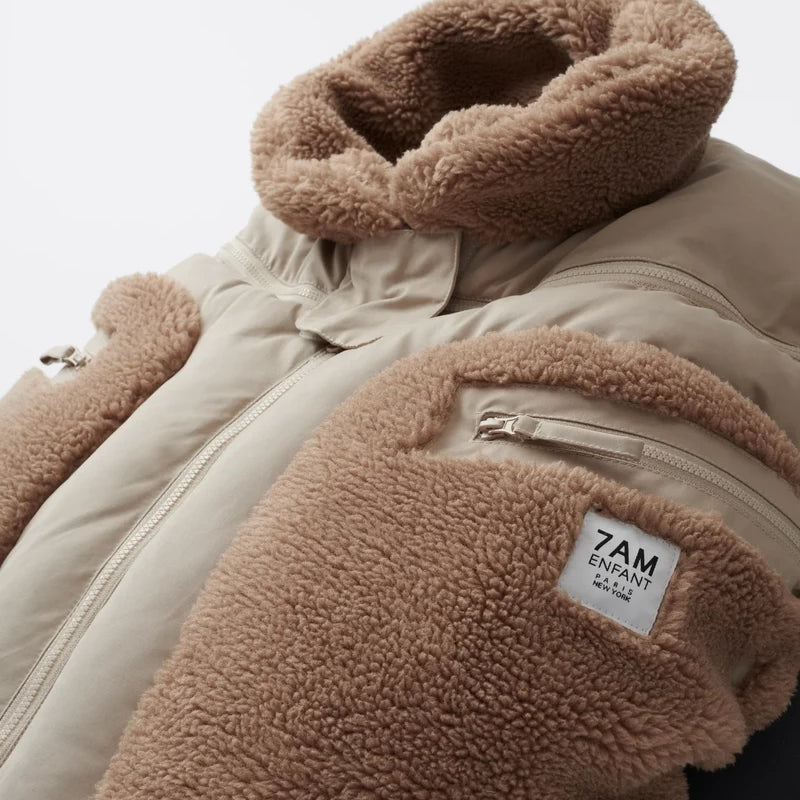 Benji Applique Car Seat Cocoon by 7AM Enfant featuring a close-up of the light taupe or oat-colored weatherproof outer shell, brown sherpa fleece trim around the collar and zippered side pocket, and a branded 7AM Enfant patch.