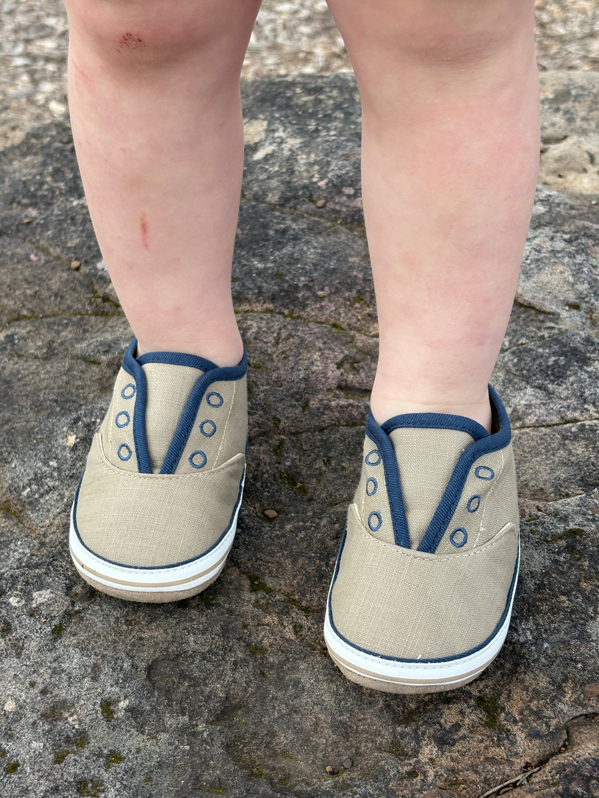 Beige shoes with blue accents worn by a child on a stone surface