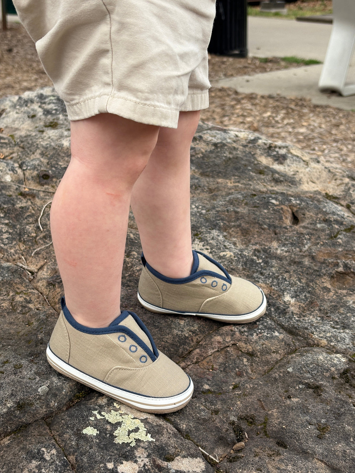 Child wearing beige sneakers with blue accents on a stone surface