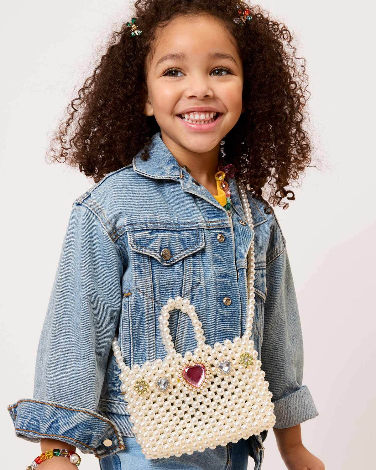 Child wearing a denim jacket holding a decorative white handbag with a heart charm on a light background