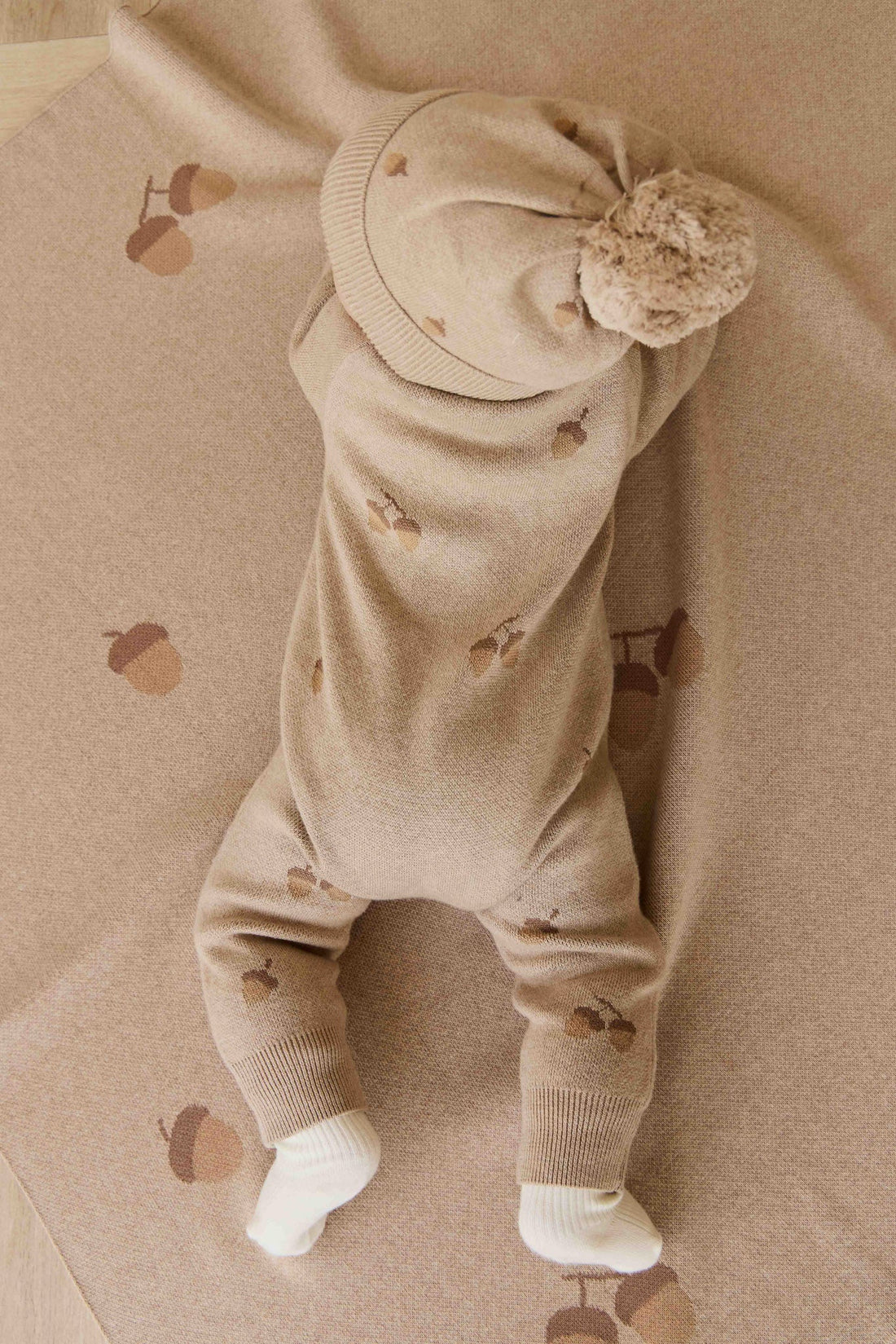 Baby in a beige outfit with matching hat and shoes on a beige background