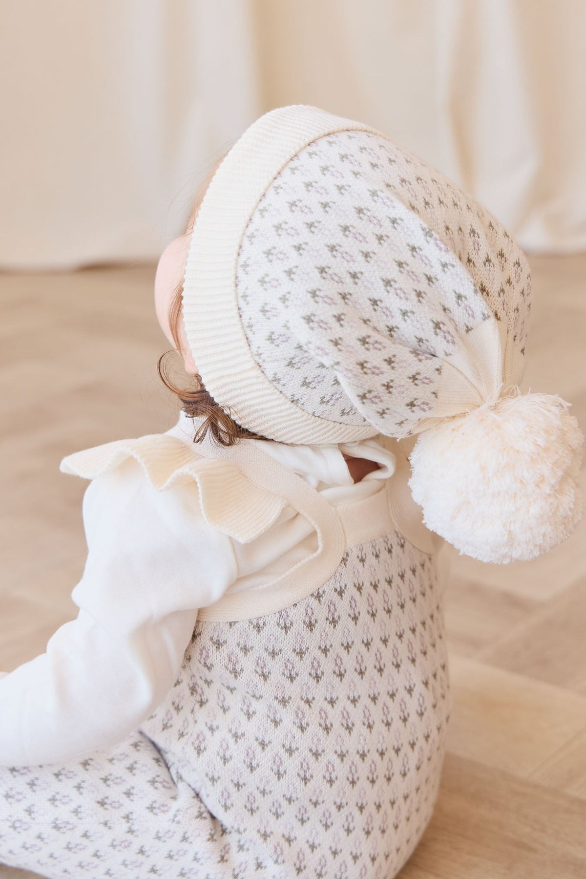 Newborn baby wrapped in a white blanket with a matching hat on a light wooden floor.