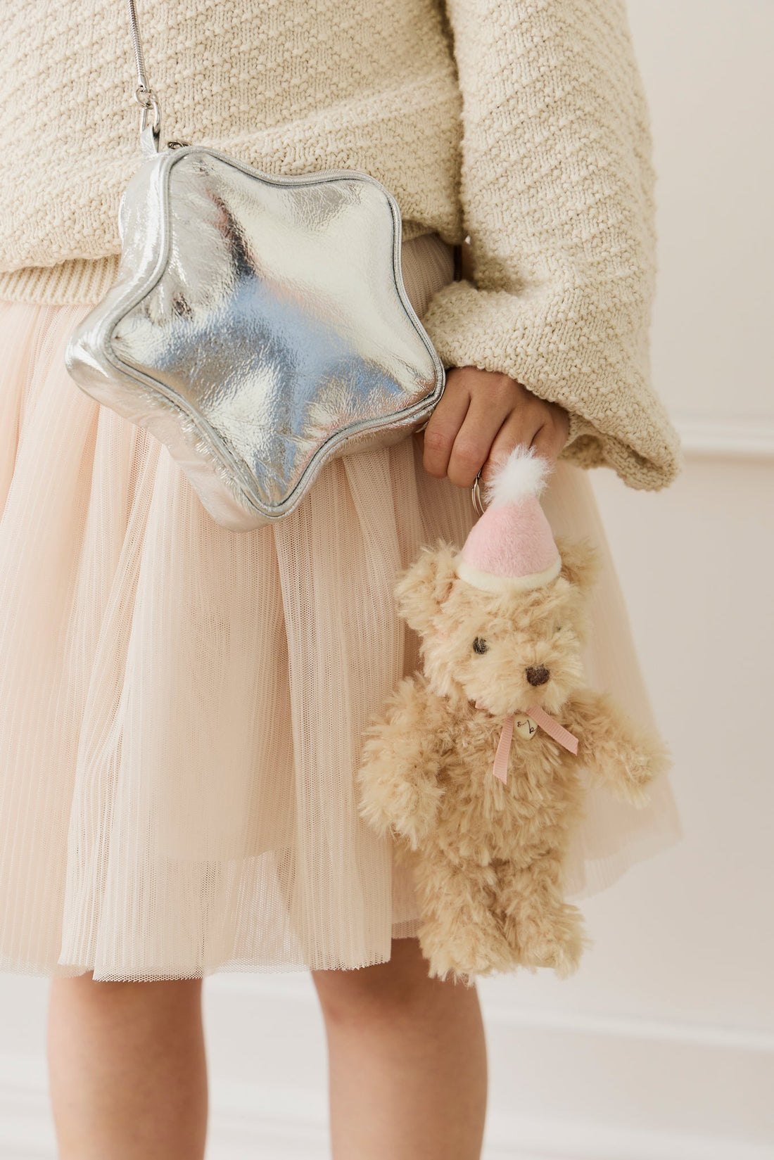 Child wearing a textured cream sweater, a pale pink tulle skirt, and holding a metallic silver star-shaped handbag, with the Snuggle Bunnies Arthur Keyring clipped to the skirt.