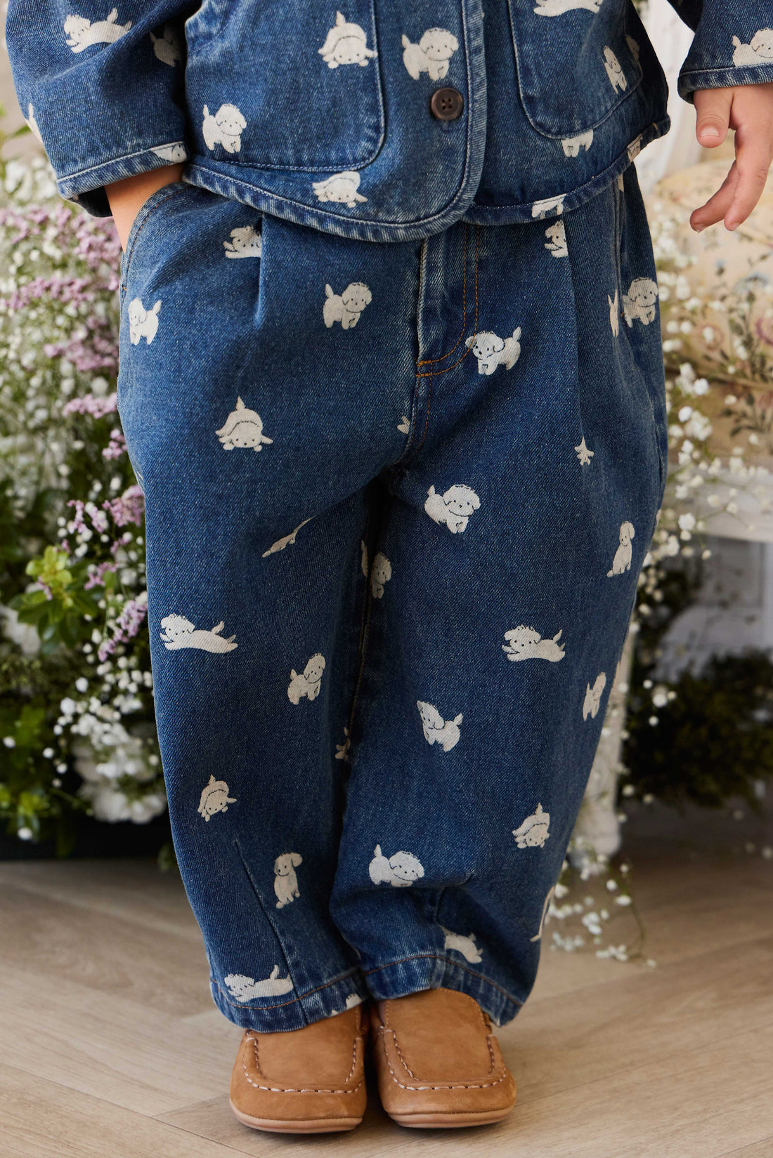 Child wearing blue jeans with white patterns and brown shoes, standing in a garden.