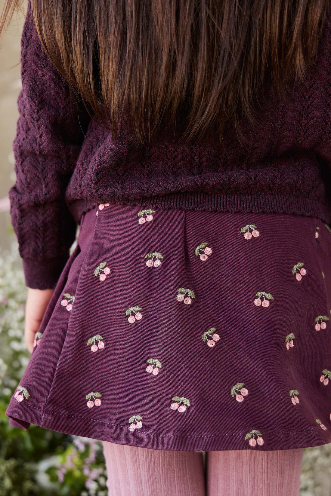 Person wearing a dark purple sweater and skirt with cherry pattern
