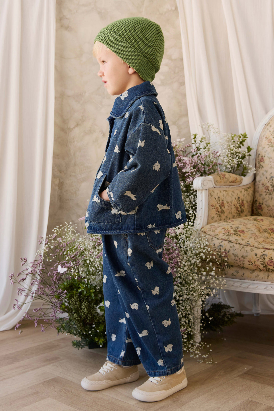Child wearing a denim outfit with bird patterns in a room with floral decorations.