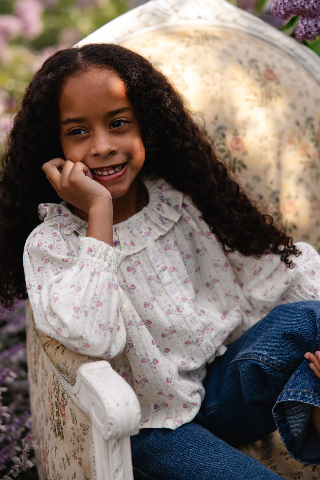 Young girl sitting on a floral-patterned chair with a blurred background