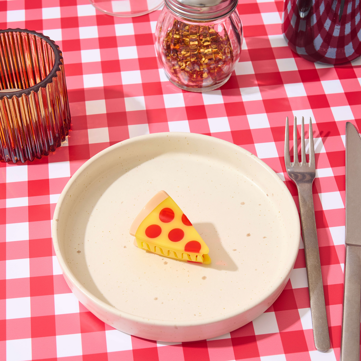 White plate with a pizza slice on a red and white checkered tablecloth