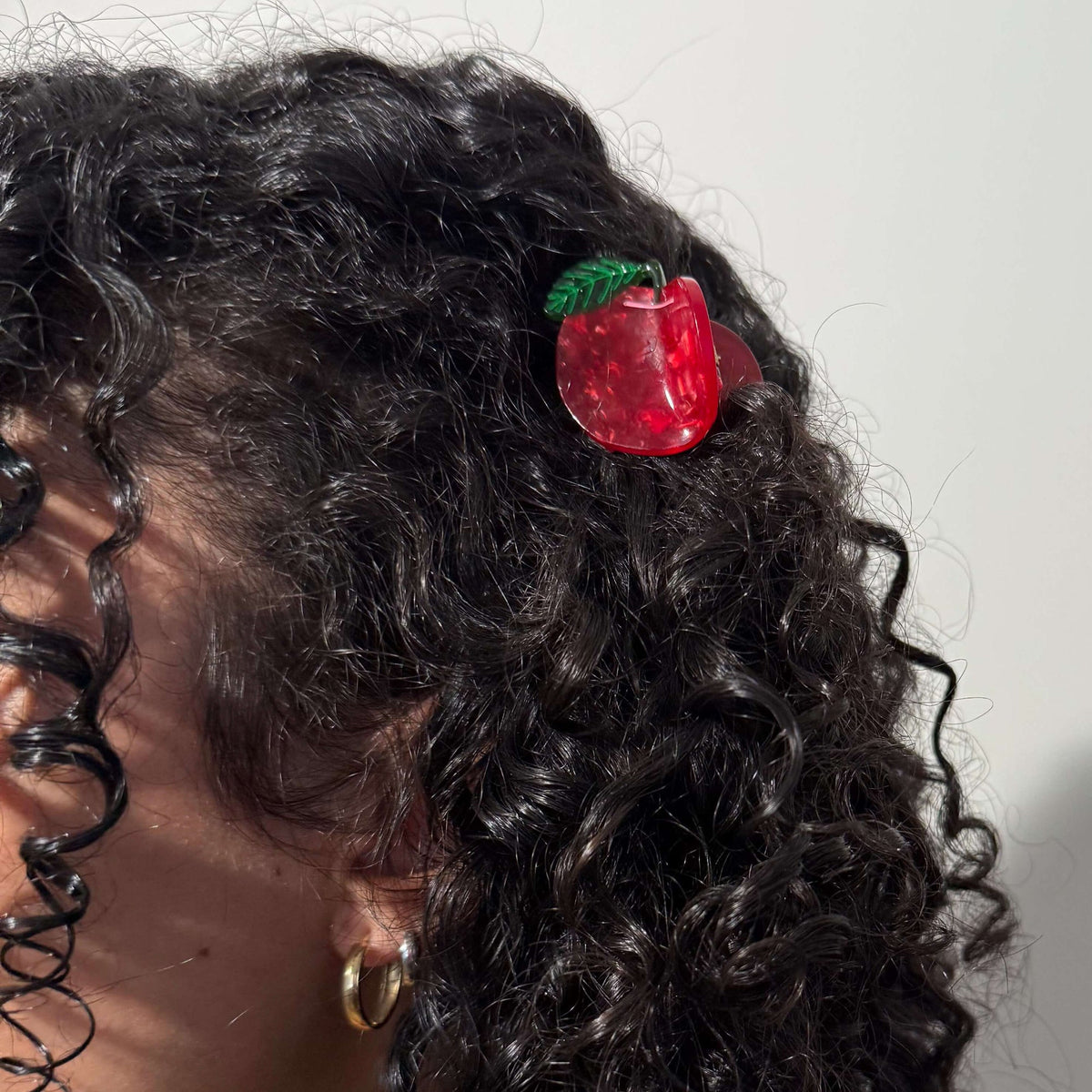Close-up of curly hair with a red apple-shaped hair clip on a plain background