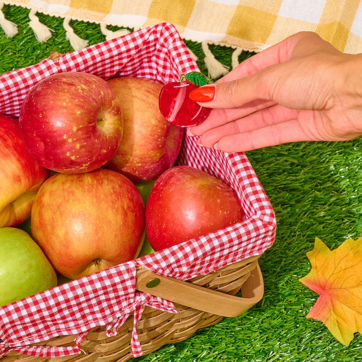 Basket of apples with a hand holding a cherry on a checkered cloth background
