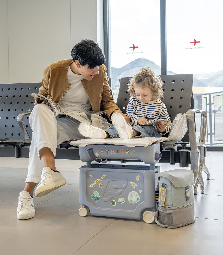 Person and child using a travel seat in an airport lounge.