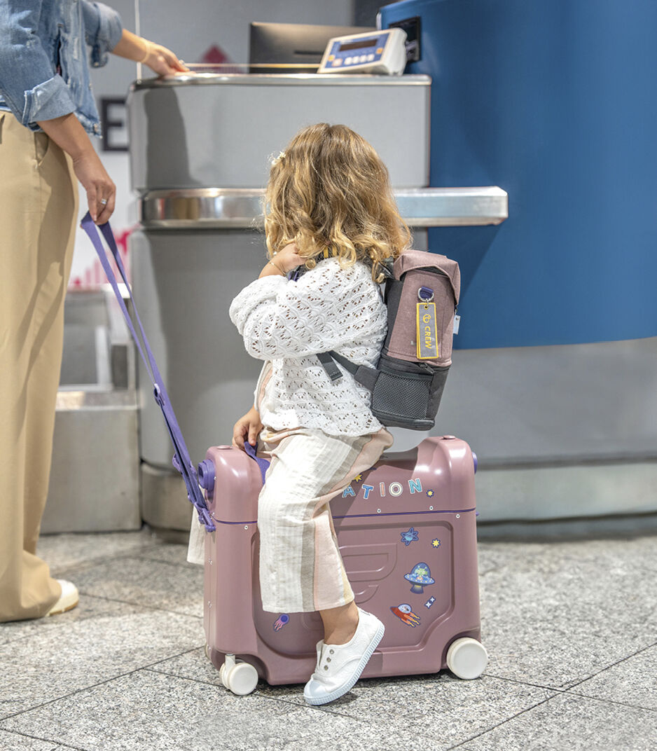 Child with a pink suitcase and backpack at an airport check-in counter.