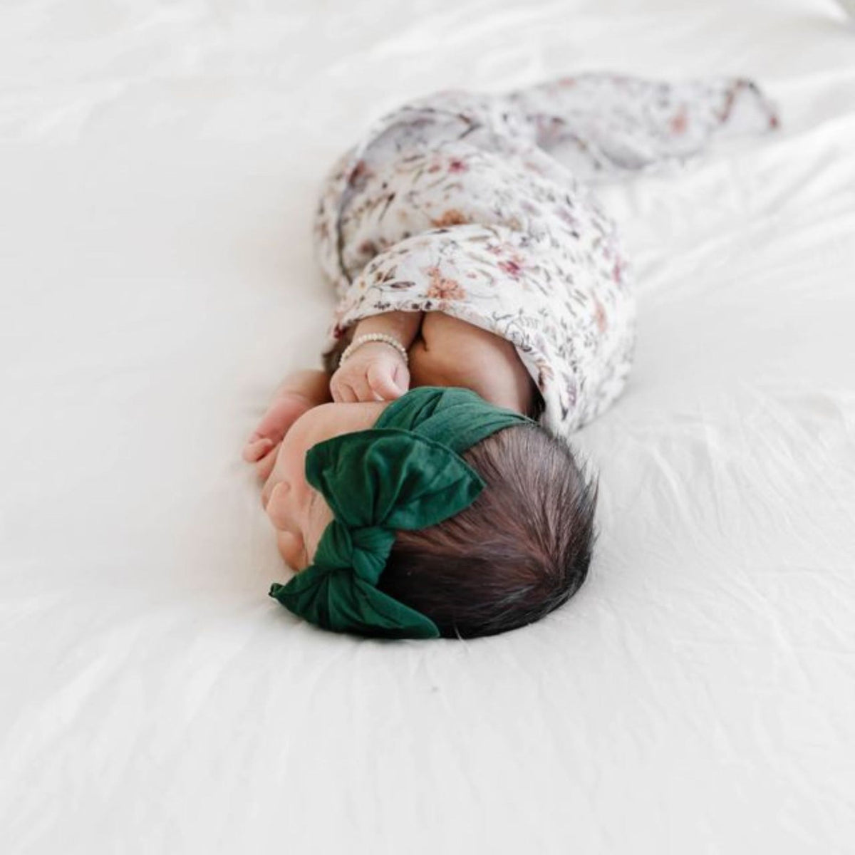 Newborn baby wrapped in a floral blanket with a green headband on a white background