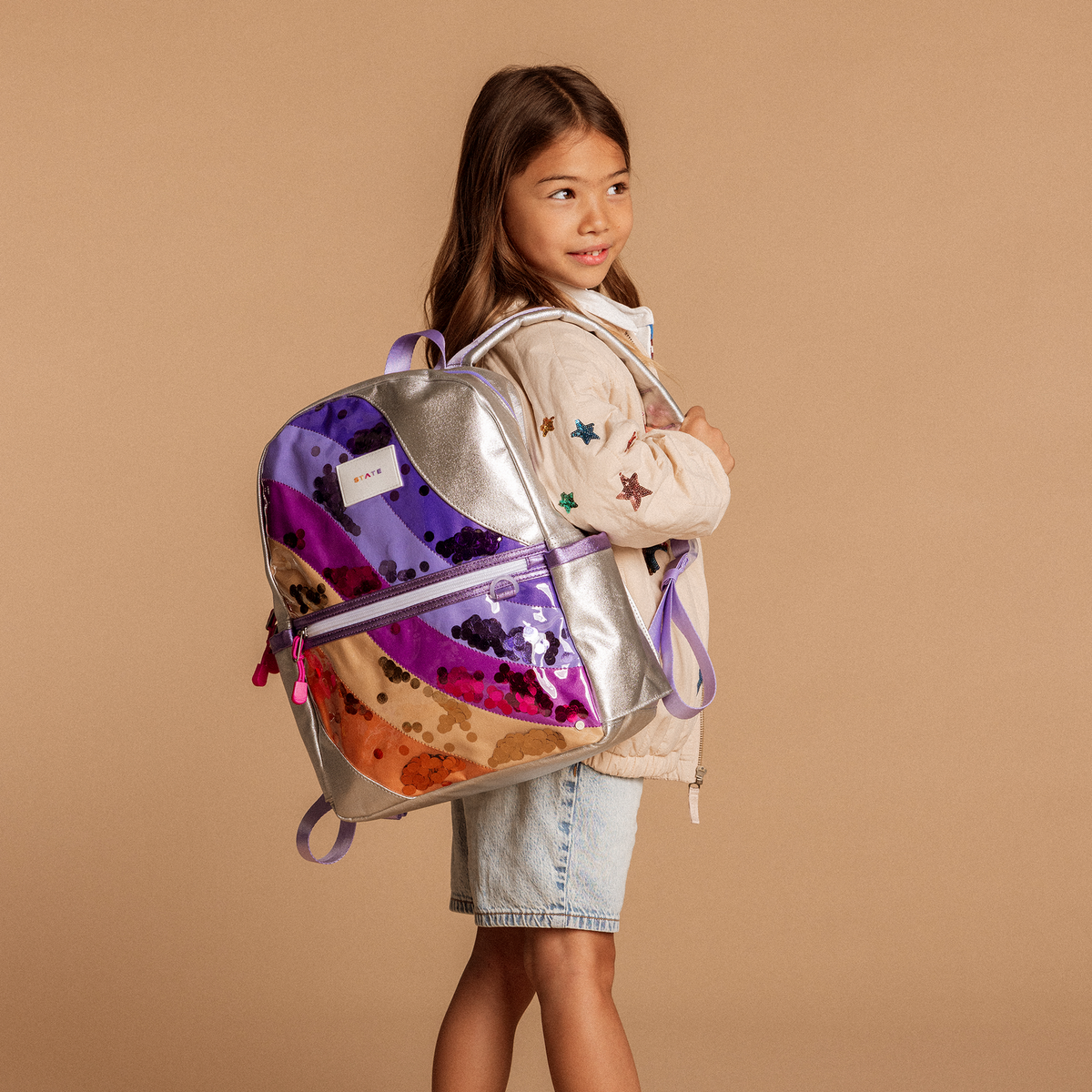 Girl with a colorful backpack on a beige background