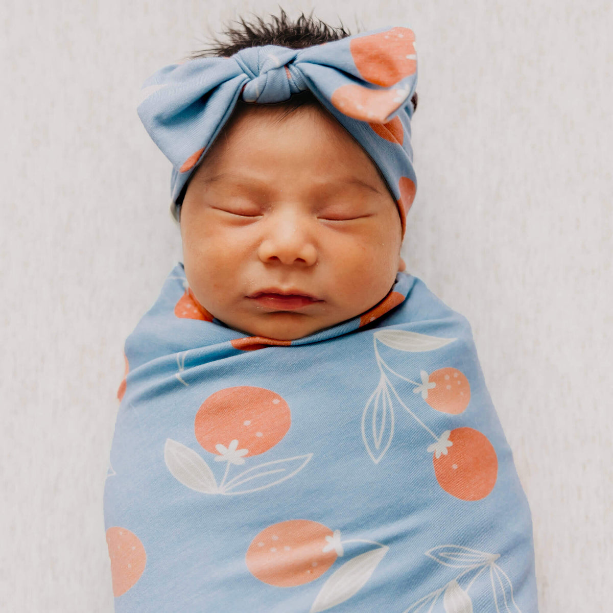 Newborn baby swaddled in a blue blanket with orange floral patterns, wearing a matching headband.
