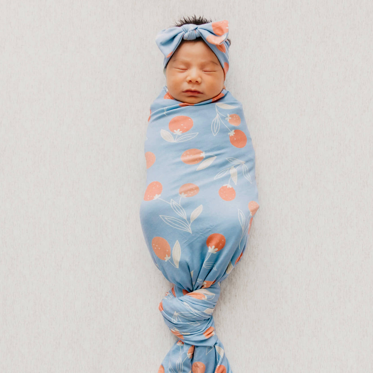 Newborn baby swaddled in a blue blanket with pink floral patterns on a plain background