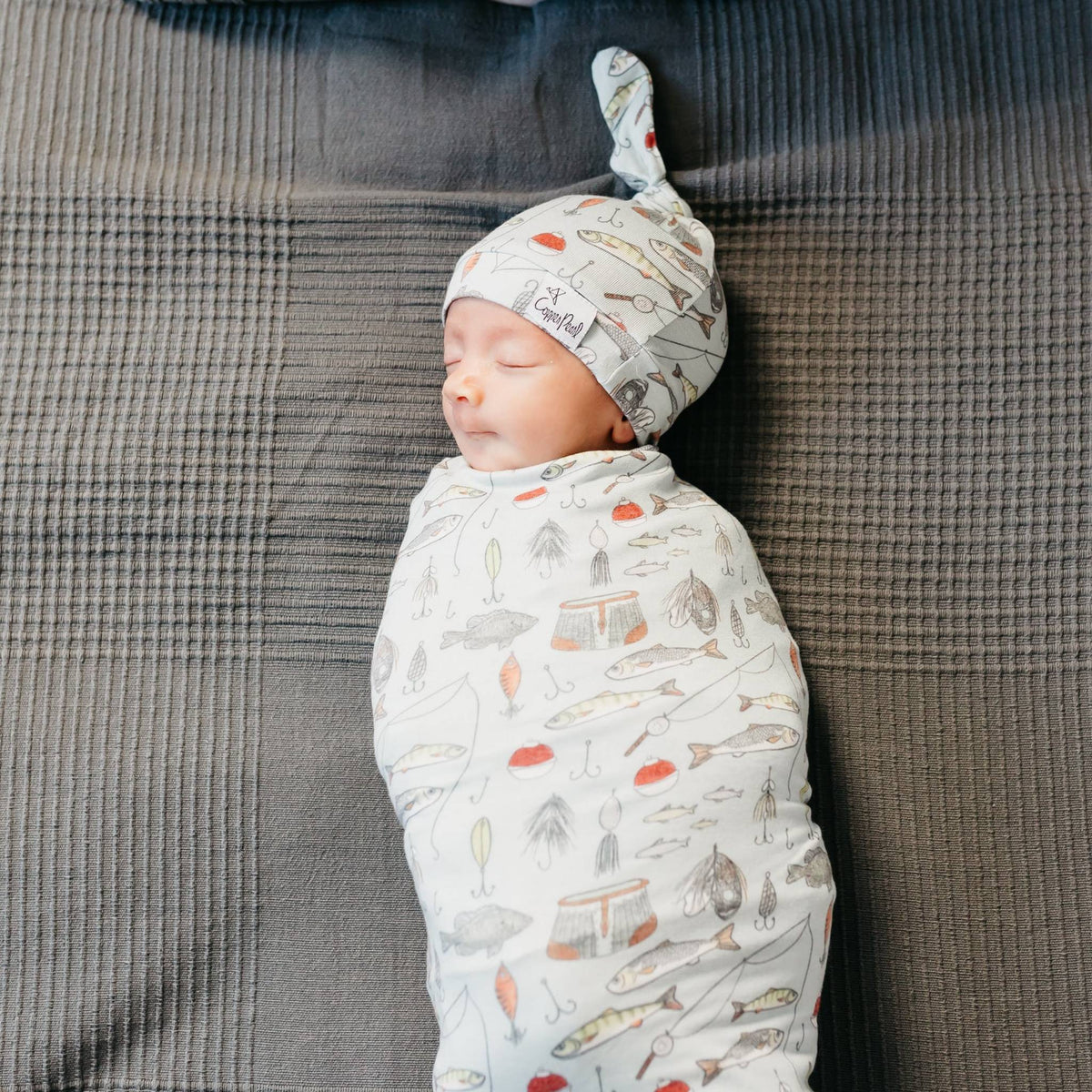 Newborn baby swaddled in a patterned blanket with a matching hat on a textured surface