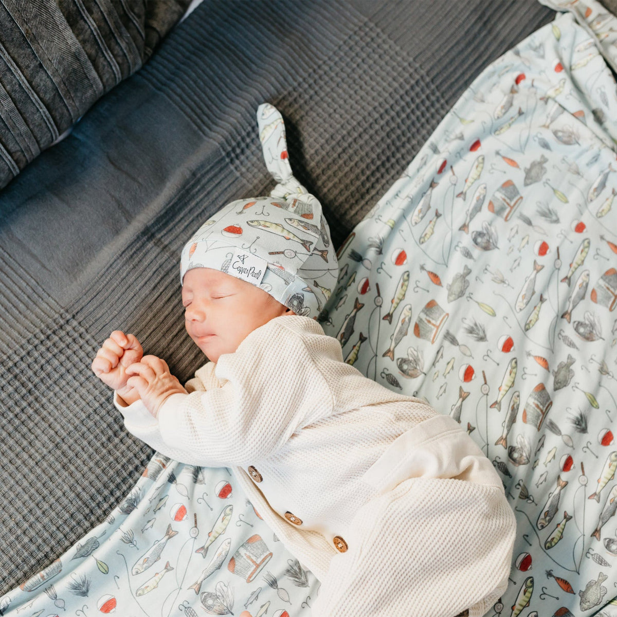 Newborn baby sleeping on a couch with a patterned blanket and hat.