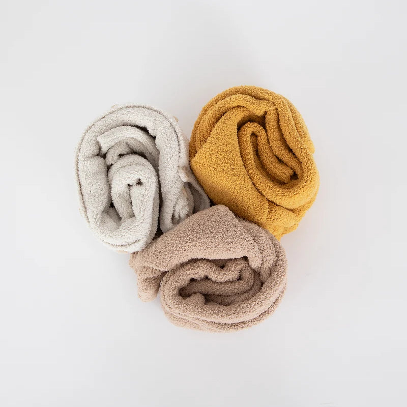 Three rolled-up fuzzy rompers by 7AM Enfant in ecru, mustard yellow, and taupe arranged together on a white background.
