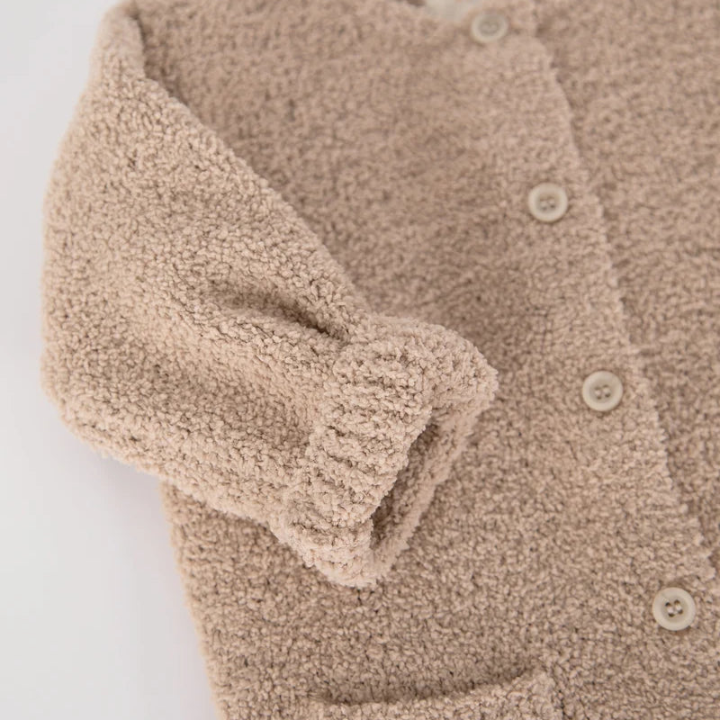 A close-up view of the upper portion of a soft, fuzzy pecan brown romper by 7AM Enfant, highlighting its round neckline, center button placket, folded-up sleeves, and front pocket against a neutral background.