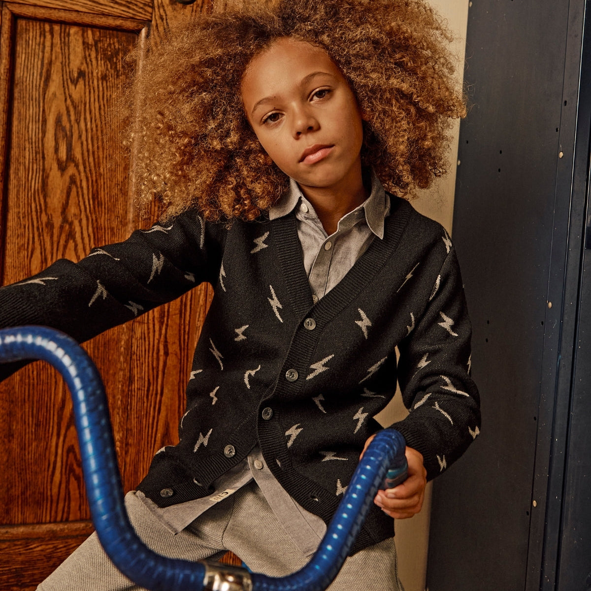 Child wearing a patterned cardigan with a bicycle indoors