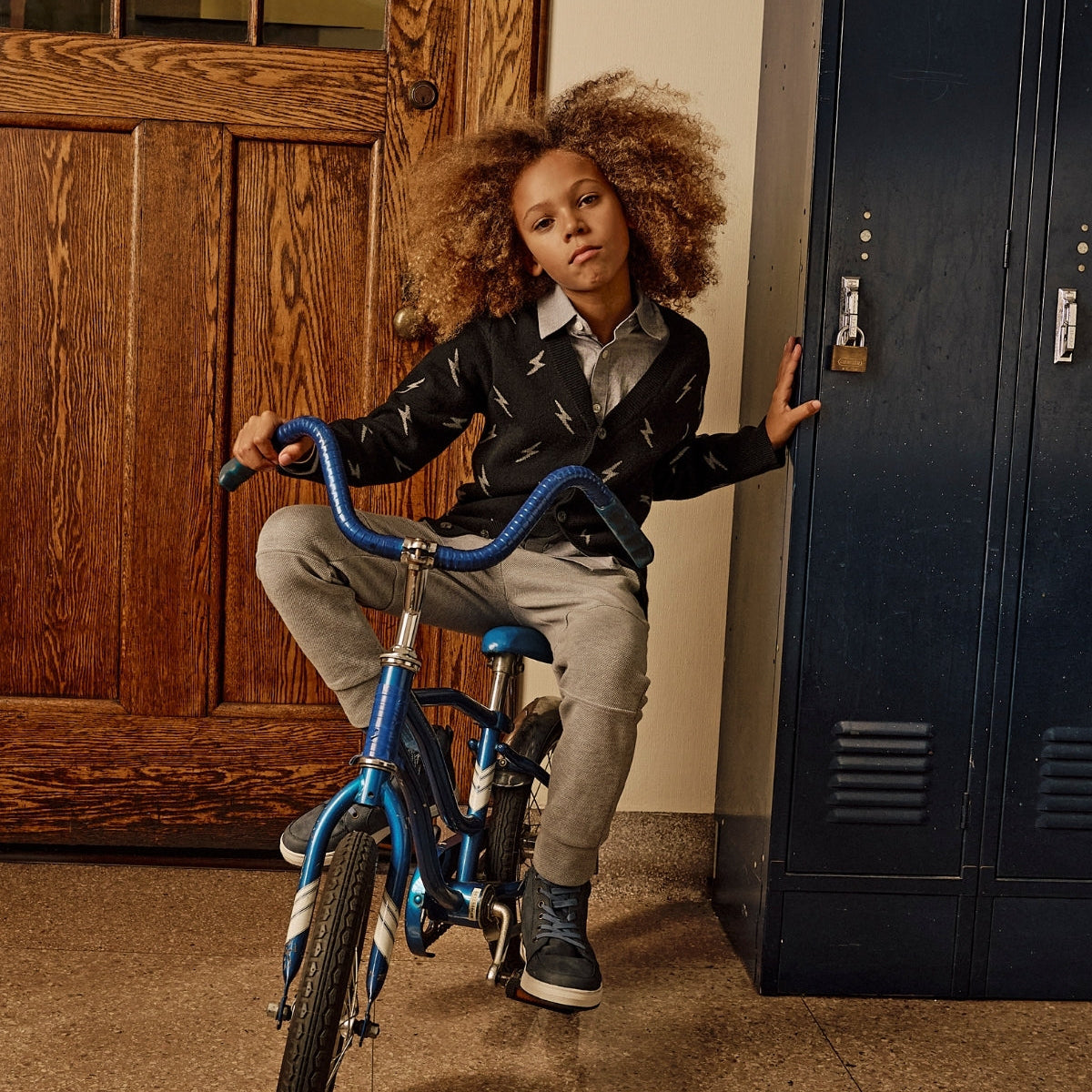 Child with a bicycle in front of a wooden door and blue locker.