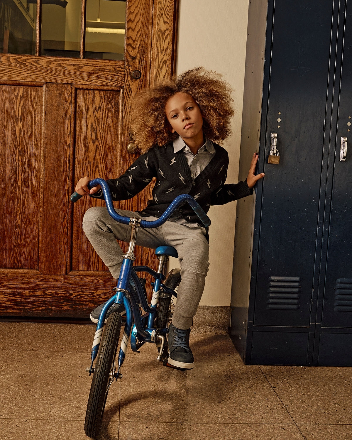 Child with a bicycle in front of a wooden door and blue locker.