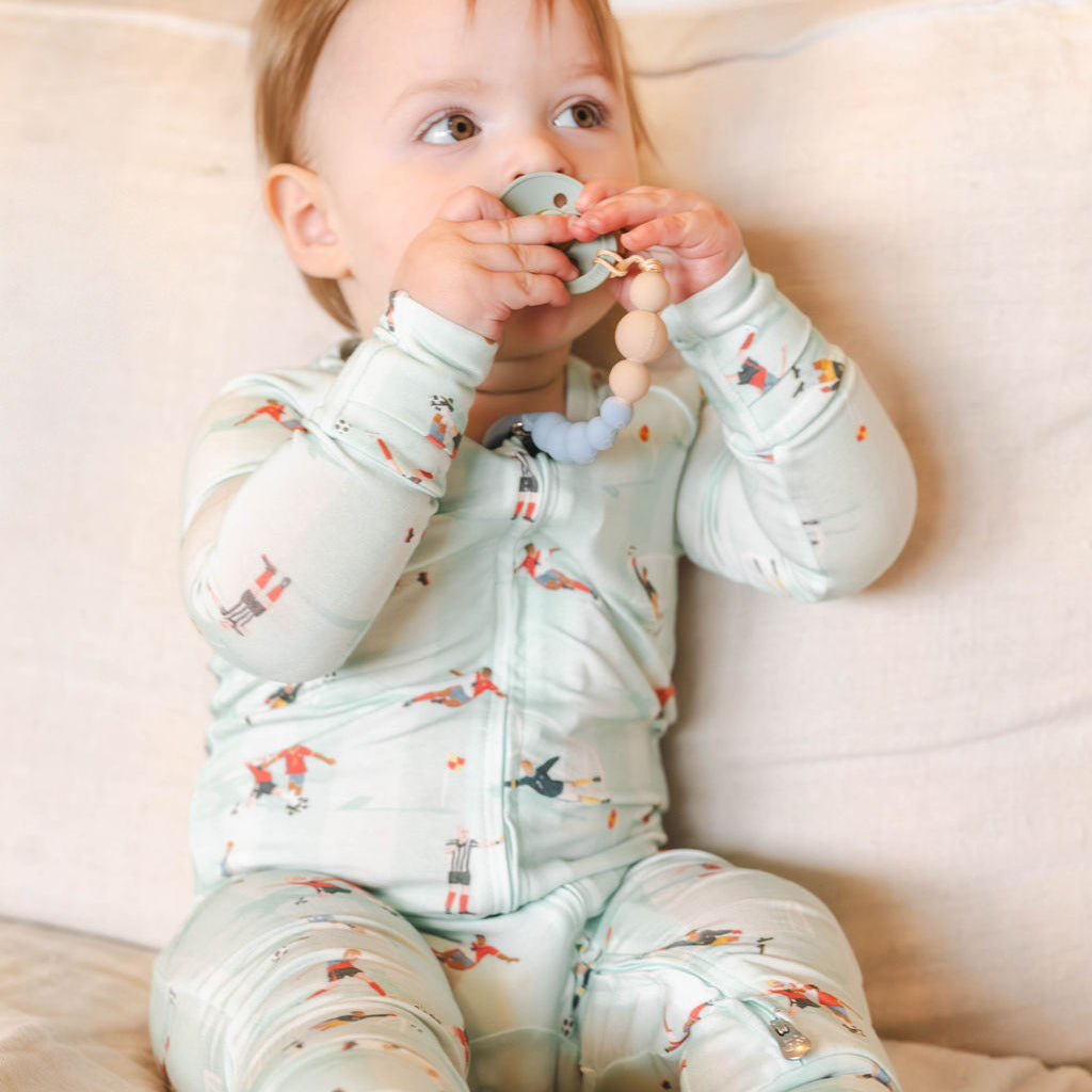 Baby in a light green onesie with bird pattern sitting on a beige couch.