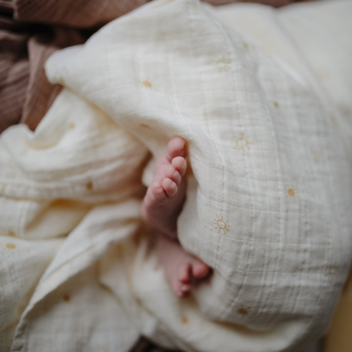 A close-up of a baby's tiny feet wrapped in a white muslin swaddle blanket.