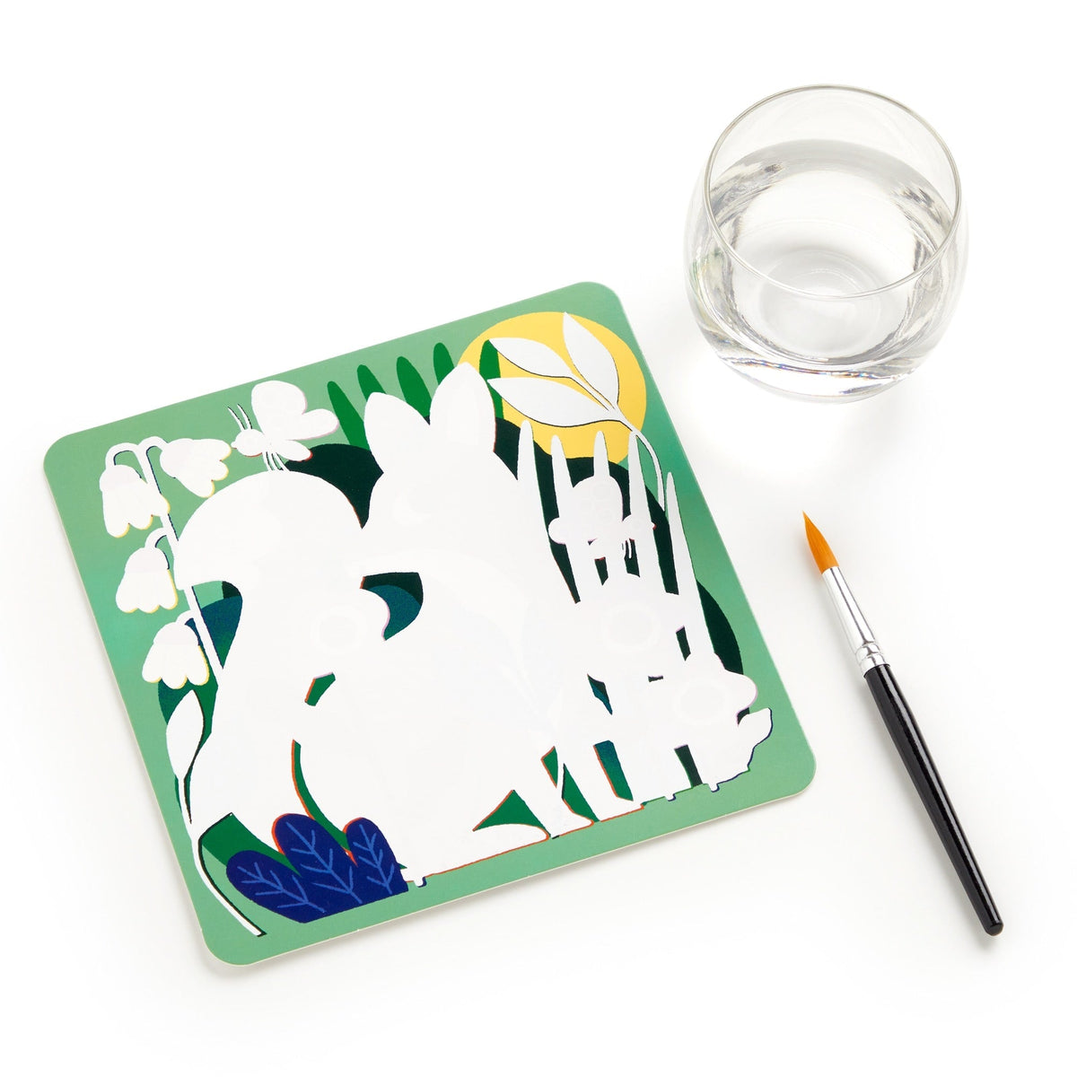 A water-reveal activity board featuring a silhouetted white squirrel and acorn design against a green background with blue leaves, acorns, and branch details. A paintbrush rests diagonally to the right next to a small clear cup of water on a white background.