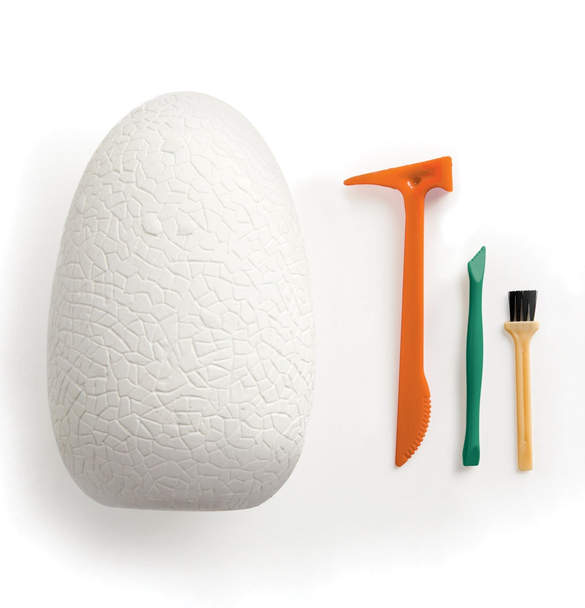 A large white textured dinosaur egg alongside three excavation tools—an orange digging tool, a green chisel, and a small yellow brush—set against a plain white background.
