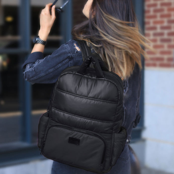 Woman wearing a black backpack outdoors near a building with a brick wall.