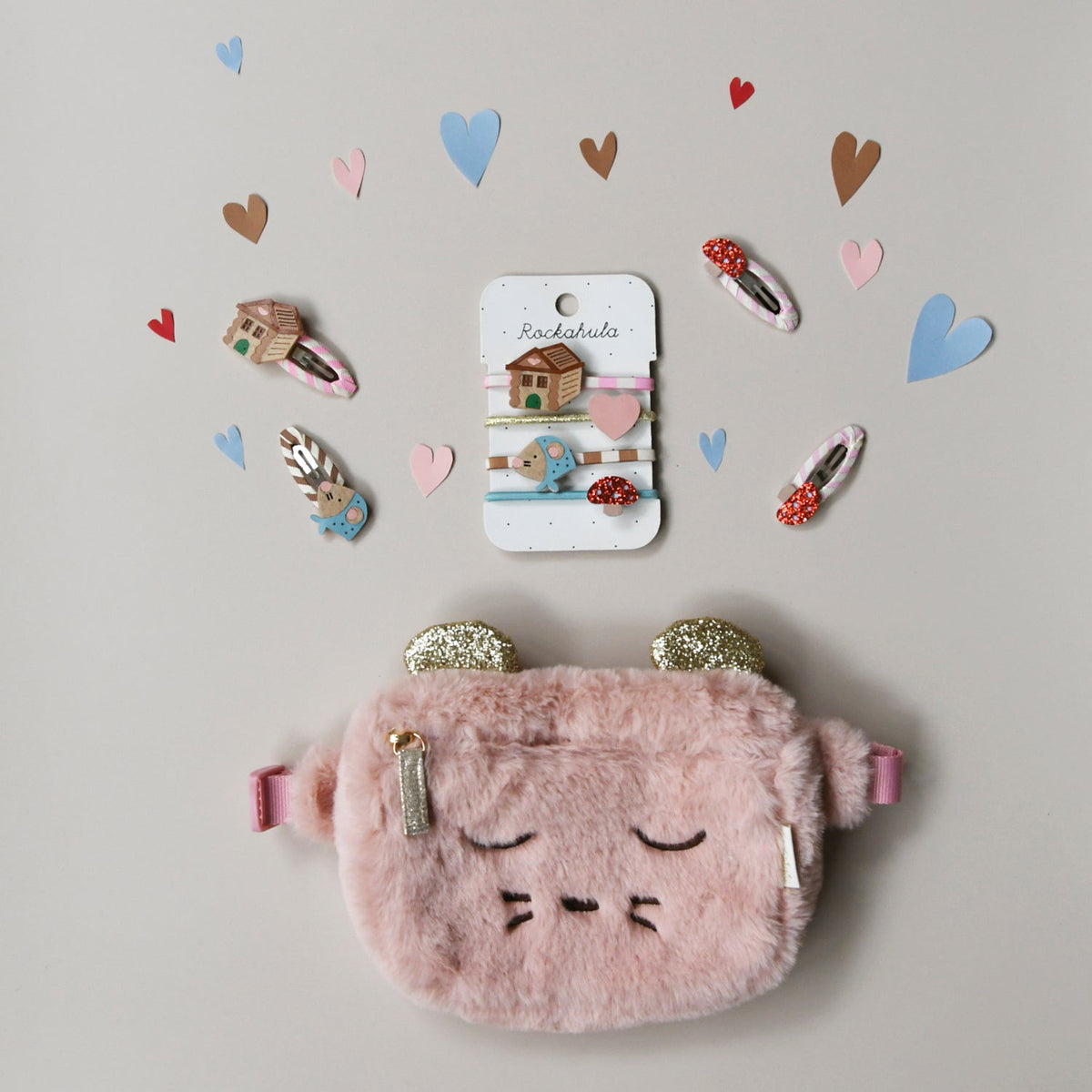 Pink fluffy pouch with gold accents and a card of hair clips on a light gray background with heart decorations.