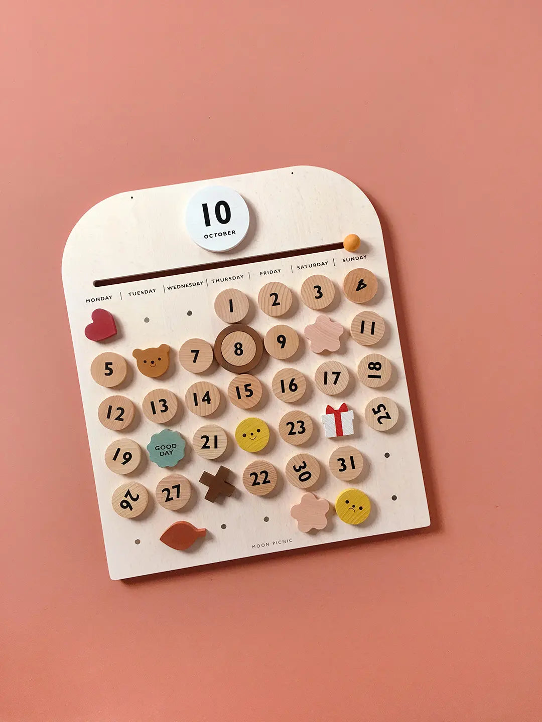 Wooden calendar with decorative numbers and symbols on a pink background