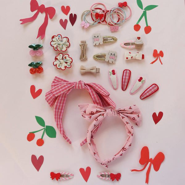 Collection of pink hair accessories including headbands, clips, and bows on a light pink background with decorative elements.
