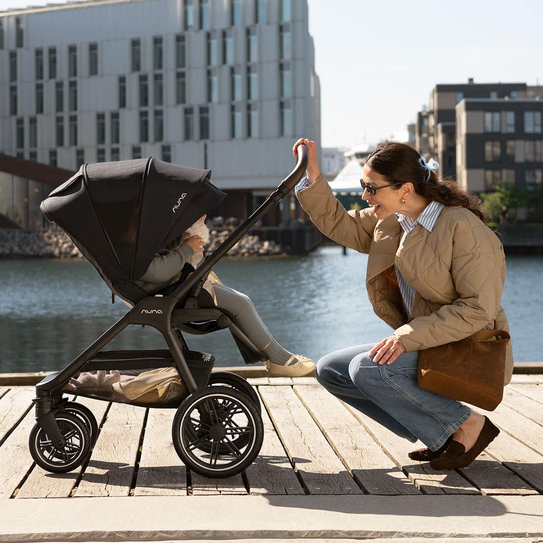 Woman pushing a stroller by a waterfront with buildings in the background