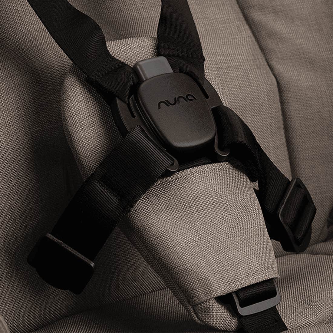 Close-up of a black seat belt buckle on a gray car seat with 'Nuna' branding.