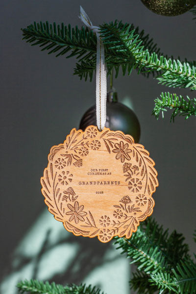 Wooden ornament with engraved design hanging on a Christmas tree branch.
